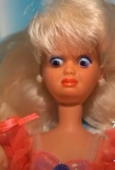 a close up of a doll with blonde hair and blue eyes wearing a red dress