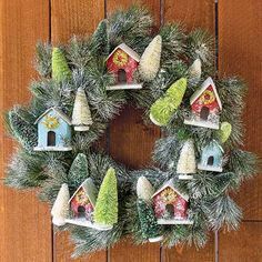 a wreath with houses and trees hanging on the side of a wooden wall in front of a door