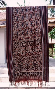 a large red and black rug hanging from a clothes line with palm trees in the background