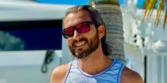 a man wearing sunglasses standing in front of a palm tree and white van with red tinted glasses