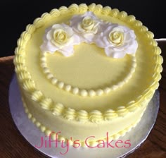 there is a yellow cake with white flowers on the top and bottom, sitting on a wooden table