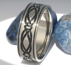 two wedding bands with black wire on them sitting next to some rocks and blue stones