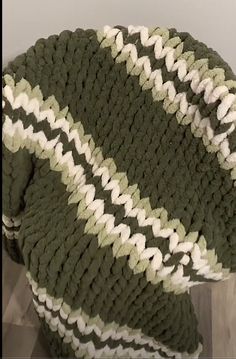 a green and white crocheted blanket sitting on top of a wooden floor next to a wall