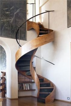 a spiral staircase with bookshelf in the middle and paintings on the wall behind it