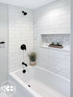 a bathroom with white tile and black fixtures in the bathtub, along with a potted succulent plant