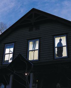 two people are seen in the windows of an old black house with snow on the roof