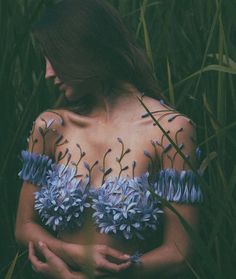 a woman with blue flowers painted on her body in the middle of some tall grass