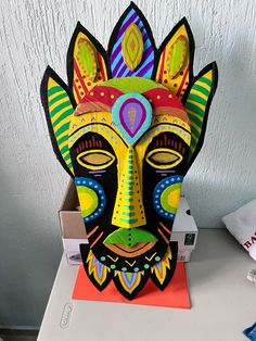 a colorful mask sitting on top of a table next to a box with an envelope