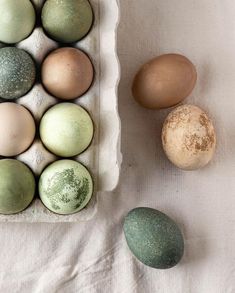 several different colored eggs in a carton on a white tablecloth next to each other