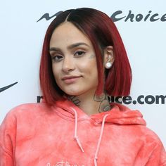 a woman with red hair and piercings wearing a pink hoodie at an event