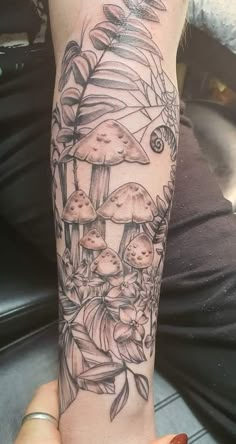 a woman's arm with tattoos on it and mushrooms in the forest behind her