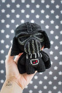 a hand holding up a small black knitted star wars darth vader toy