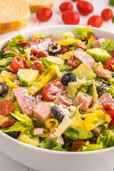 a salad with ham, olives, tomatoes and parmesan cheese in a white bowl