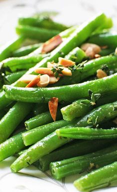 a white plate topped with green beans covered in nuts and seasoning on top of it