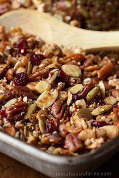 a bowl filled with nuts and cranberries next to a wooden spoon