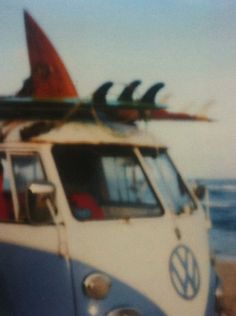 an old van with surfboards on top is parked in front of the ocean and waves