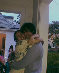 two people hugging each other in front of a house