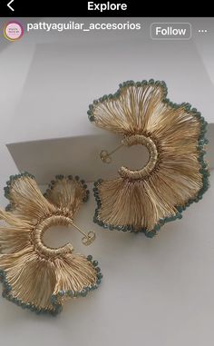 two pairs of gold and green earrings on top of a white table next to a card