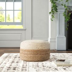 a white and brown ottoman sitting on top of a rug in front of a window