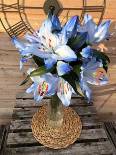 a vase filled with blue flowers sitting on top of a wooden table next to a wicker basket