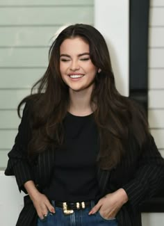 a woman with long hair and black shirt standing in front of a white wall smiling