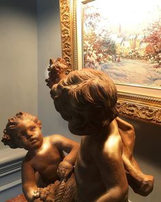 a statue of a boy and a girl in front of a painting