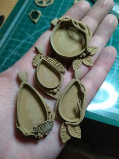 three pieces of carved clay in the palm of someone's hand, some with leaves on them