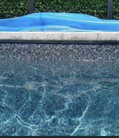 an empty swimming pool next to a hedge with blue tarp on it's edge