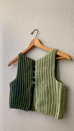 two knitted vests hanging on a wall next to a hanger with clothes