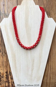 a red beaded necklace sitting on top of a wooden board next to a white piece of wood