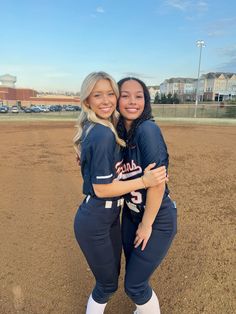 two softball players hugging each other on the field in front of an empty baseball field