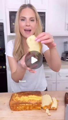 a woman holding up a piece of bread on top of a wooden cutting board next to a knife