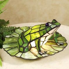 a stained glass frog sitting on top of a table next to a potted plant