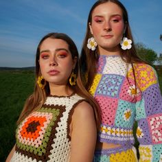 two young women standing next to each other in front of a green field and blue sky