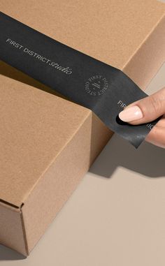 a woman's hand holding a piece of black paper in front of a cardboard box