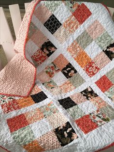 an orange and white quilt on top of a wooden chair next to a blanket that has flowers on it