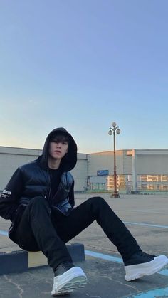 a young man sitting on top of a cement bench wearing a black jacket and white sneakers