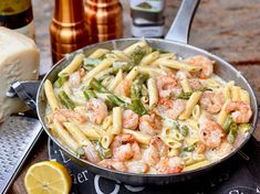 pasta with shrimp and asparagus in a skillet next to sliced lemons