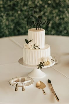 a white wedding cake sitting on top of a table next to silver utensils