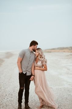 a man and woman standing next to each other on a dirt road in front of the ocean