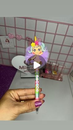 a hand holding a toothbrush with a cartoon doll on it's head in front of a bathroom sink