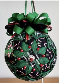 a green christmas ornament hanging from a metal stand with ribbon and candy canes on it