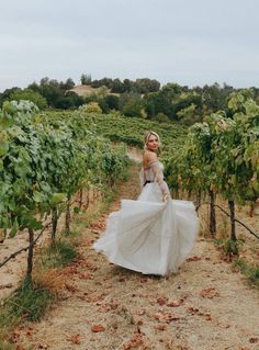 a woman in a white dress is walking through the vineyard