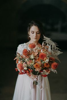 a woman in a white dress holding a bouquet of orange and red flowers with her eyes closed