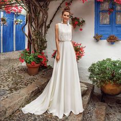 a woman standing in front of a building wearing a white dress and flower potted plants