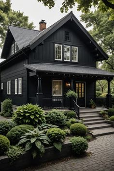 a black house with white windows and lots of greenery on the front porch, along with steps leading up to it