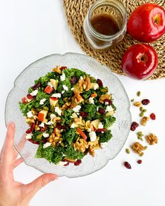 a person holding a glass plate with salad on it next to an apple and some nuts