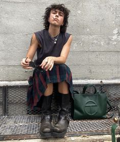 a woman sitting on a bench next to a green handbag and her legs crossed