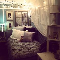 a bed sitting under a white curtain next to a night stand with lights on it