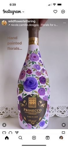 the bottle is decorated with purple flowers and has a brown wooden cap that says, hand painted florals